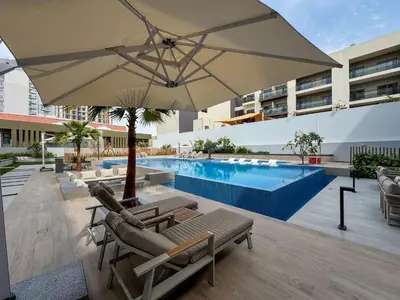 a pool with chairs and an umbrella next to a pool at Luxury Loft with Balcony in JVC, Oxford Terraces 2 in Dubai
