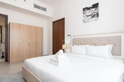 a bedroom with a large white bed and a wooden cabinet at Delightful 2 Bedrooms In Jumeirah Village Circle in Dubai