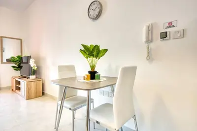 a dining room table with white chairs and a clock on the wall at Posh Studio Apartments in Dubai