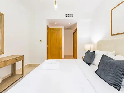 a white bedroom with a white bed and a wooden table at Cozy 1BR- Yansoon 4- Heart of Downtown Dubai in Dubai