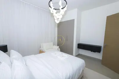 a white bedroom with a white bed and a chandelier at Sobha Hartland Waves-912 in Dubai