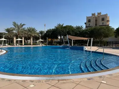 a large blue swimming pool with palm trees and a building at New 1BED Apartment in Remraam, Dubai Land, Motor city, Damac hills, Mudoon area in Dubai