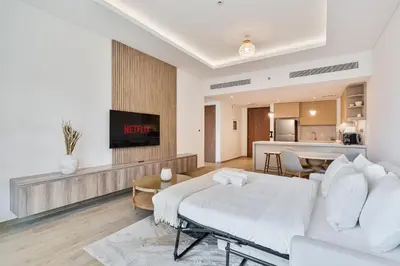 a living room with a white bed and a kitchen at Chic 1BR APT with Pool, Gym & Kid's Playground in Dubai