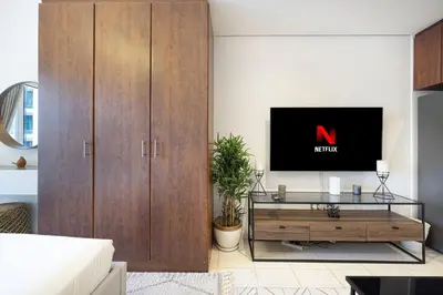 a living room with a tv and a wooden cabinet at Lake View Studio near Marina with Pool, Balcony and Gym in Dubai