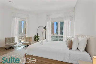 a white bedroom with a large white bed and windows at Spacious refurbished Studio steps away from metro in Dubai