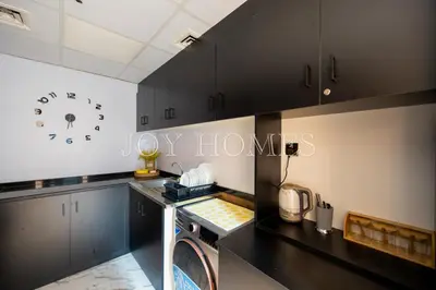 a kitchen with black cabinets and a clock on the wall at Amiralty Easy Stay in Dubai