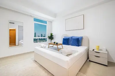 a white bedroom with a large bed with blue pillows at Prime Location - 2BR with Spectacular Sea View in Dubai
