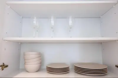 a white kitchen with plates and wine glasses on a shelf at Charming 1 Bedroom Apt in MBR - Near Downtown Dubai in Dubai
