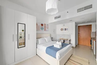 a white bedroom with a bed and a mirror at Modern Studio in Production City in Dubai