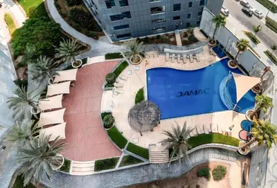 an overhead view of a pool with palm trees and a building at Spacious 1BR - Balcony & Pool View - Capital Bay in Dubai