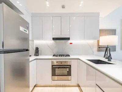 a kitchen with white cabinets and a stainless steel refrigerator at TRPS - Binghatti Emerald, Jumeirah Village Circle - Luxury 1BR Haven in Dubai