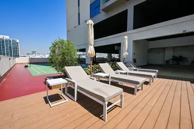 a row of lounge chairs and a tennis court on a building at Stylish 1BR Apartment - Central Location in JVC - Balcony - Holiday Boulevard in Dubai