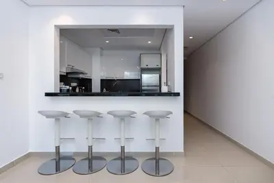 a kitchen with a bar with four stools in it at Silverene Tower - One Bedroom By Home Of Choice in Dubai