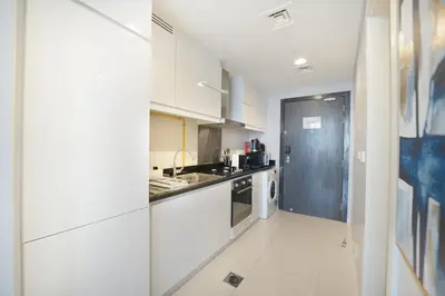 a white kitchen with a sink and a stove at EasyGo- Sleek Studio at Damac Hills Artesia D in Dubai