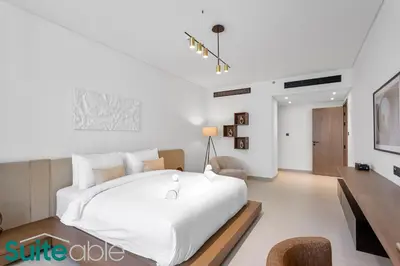 a white bedroom with a large white bed and a chair at Sophisticated 1 Bedroom in Binghatti Galaxy JVC in Dubai