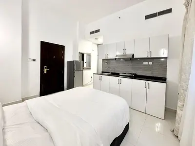 a white bedroom with a large bed and a kitchen at Al Manara Classic Executive Studio in Dubai