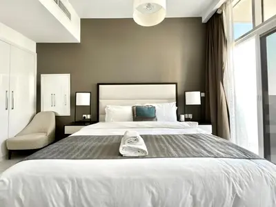 a bedroom with a large white bed and a chair at Homes2Retreat - Chic & Cozy Studio in Damac in Dubai
