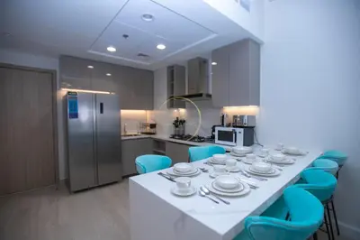 a kitchen with a white table and blue chairs at 3BHK Apartment located in Azizi riviera 34 in Dubai