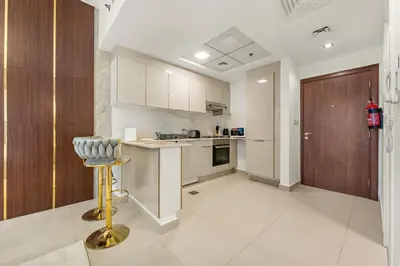a kitchen with white cabinets and a bar stool at Modern Compact Studio in JVC in Dubai