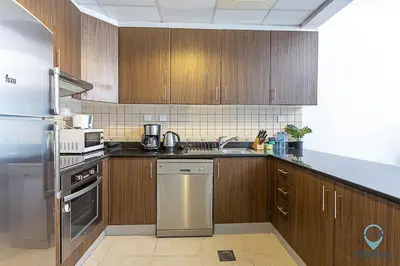 a kitchen with wooden cabinets and stainless steel appliances at 1BR Tropical Vibes Near Skydiving and Beach! in Dubai