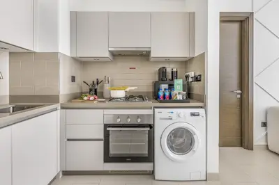 a kitchen with white cabinets and a washer at New 2BR with BBQ Area, Pool in Sobha MBR City in Dubai