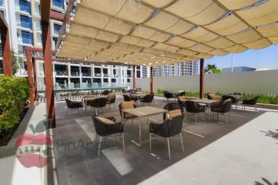 a patio with tables and chairs under a large umbrella at Stylish studio in Azizi 42 in Dubai