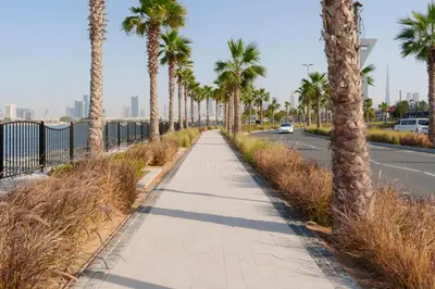 a sidewalk with palm trees on the side of a road at High-End Luxury 1BR in Port De La Mer near J1 Beachfront, Dubai in Dubai