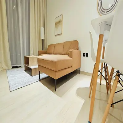 a living room with a brown couch and a tripod at Luxurious Belvilla 1BR JVC with Pool, Gym & BBQ Access in Dubai