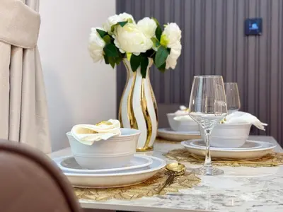 a table with a vase of white roses and a vase of glasses at Brand New-Fully Furnished Elegant 1BR In JVC in Dubai