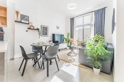 a dining room and living room with a table and chairs at Balcony Offering Community Views 1BR with Assistant Room, Walking Distance to Community Park , Pantheon Elysee , Jumeirah Village Circle by Deluxe Holiday Homes in Dubai