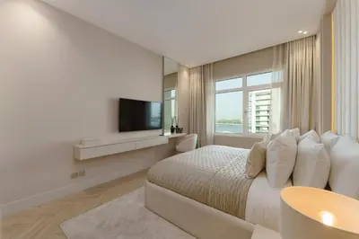 a white bedroom with a bed and a television at Daniels 1BR at Shoreline with Sea View in Dubai