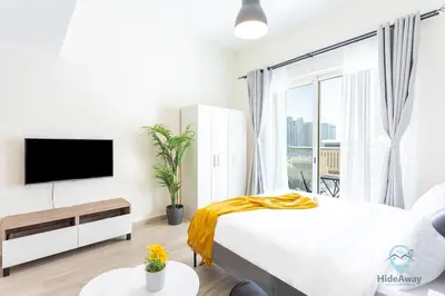 a white bedroom with a large bed and a tv at Lovely Cozy Studio l Steps to JBR in Dubai