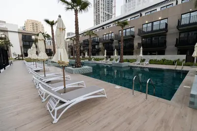 a pool with chairs and umbrellas next to a building at Chic 2BR in Oakley Square Residence, JVC in Dubai