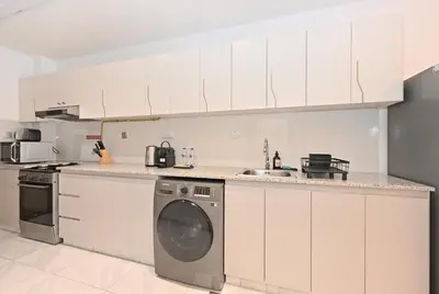 a kitchen with white cabinets and a washing machine at Stylish Escape with Balcony, Canal and Burj Khalifa Views Near Dubai Mall in Dubai