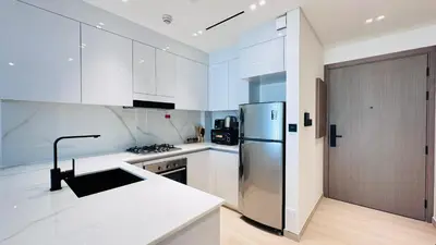 a kitchen with white cabinets and a stainless steel refrigerator at Premium 1 Bed Apartment In Binghatti Venus in Dubai
