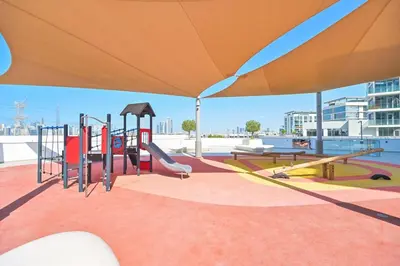 a playground with an orange umbrella and swings at Stunning 1 Bdr Luxury District one in Dubai
