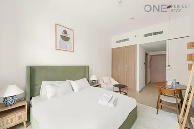 a bedroom with a large white bed and a desk at Cozy Studio Apartment in Meydan in Dubai