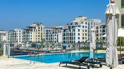 a large building with a swimming pool with chairs and an umbrella at Peaceful 1BR in La Serine, Lush Garden Views - 1AB02 in Dubai