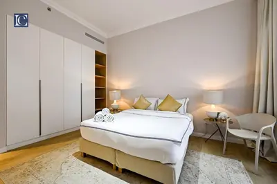 a white bedroom with a bed and a chair at Luxury Escapes - Stylish 2-Bedroom Haven in La Cote, Port de La Mer in Dubai