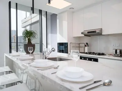 a white kitchen with a counter with plates and wine glasses at Stylish JVC 1 Bed with Wraparound Balcony in Dubai