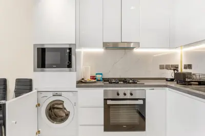 a white kitchen with a washer and a dishwasher at Chic One-Bed Haven w Pool & Gym Heart of Dubai in Dubai