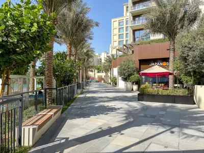 a sidewalk with palm trees and a building at Vibrant 1BR With Airy Patio, Beach, Pool and Gym Access in Dubai