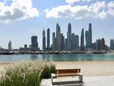 a bench sitting on the beach with a view of a city at Trophy-Sunset Coral Retreat Beachfront Living in Dubai