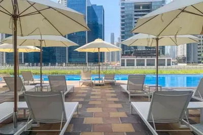a pool with chairs and umbrellas on a patio at City and Burj Khalifa View 2BR, Near Dubai Water Canal, Vera Tower, Business Bay by Deluxe Holiday Homes in Dubai