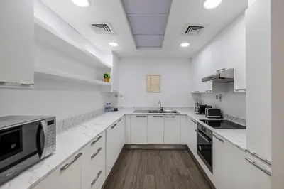 a white kitchen with white cabinets and a wooden floor at 1BR plus Extra Bedroom Bay Square B7, City View in Dubai