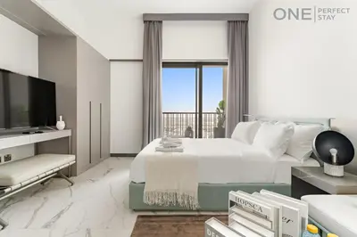 a white bedroom with a large bed and a tv at Modern Cozy Studio in Dubai