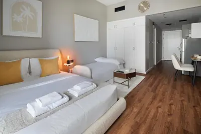 a bedroom with a large white bed and a living room at Studio Nova at Dubai Sports City in Dubai