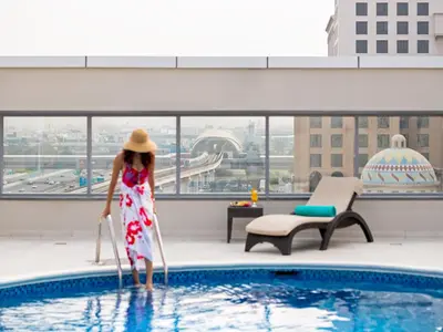 a woman in a hat standing next to a swimming pool at Flora Al Barsha Hotel At The Mall in Dubai