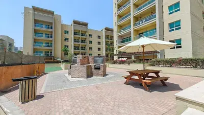 a picnic table and an umbrella in front of a building at Vogue The Greens Al Alka near Mall of the Emirates, One Bedroom Apartment with Balcony and Vibrant community View, Access to all Amenities in Dubai