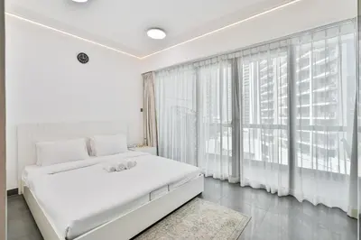 a white bedroom with a large bed and a large window at Stylish 2BR with Pool, Gym, Sauna & Kid's Playground in Dubai